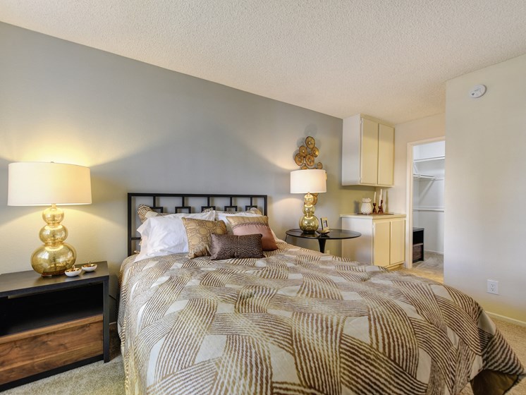 Model home bedroom with larger bed, side tables with decorative wall art. There is plush carpeting in the bedroom and built-in storage cabinets in the corner.